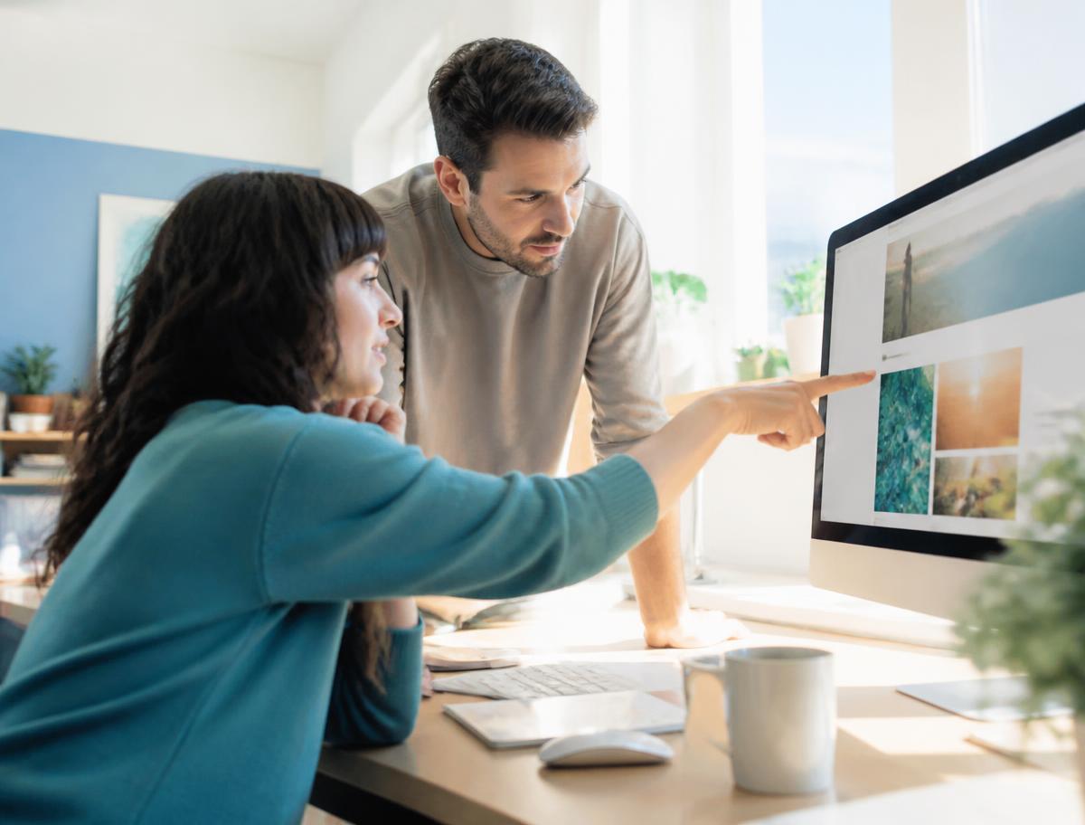 Two colleagues reviewing a website together on a large monitor, one pointing at the screen.